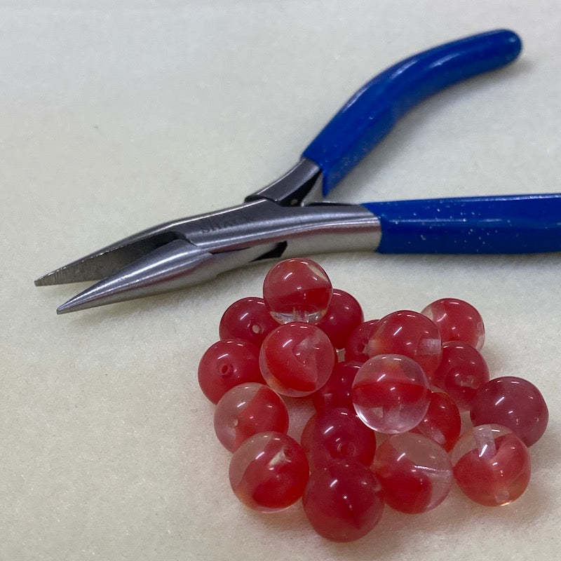 close up photo of a group of tomato red givre glass beads on a brown surface with a plier for scale