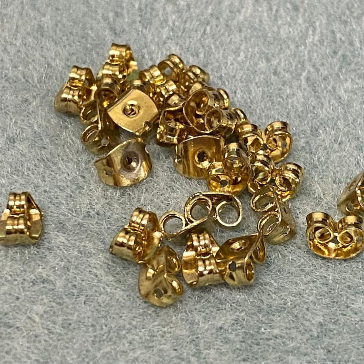 a group of gold ear ring stud backings on a textured surface