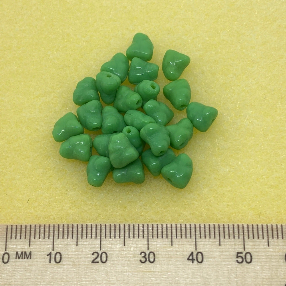 A collection of apple green opaque colored Czech glass beads with an organic, nugget-like shape with a ruler to show scale on a yellow background