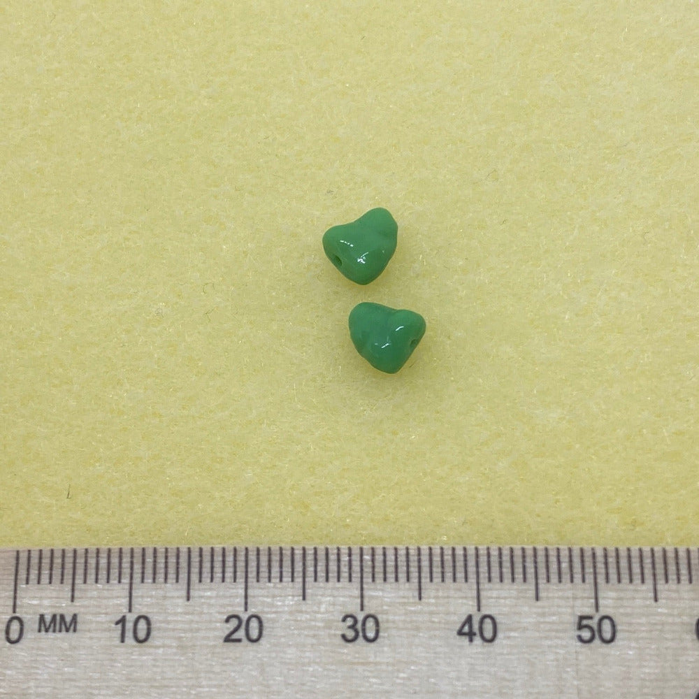two apple green opaque colored Czech glass beads with an organic, nugget-like shape with a ruler for scale