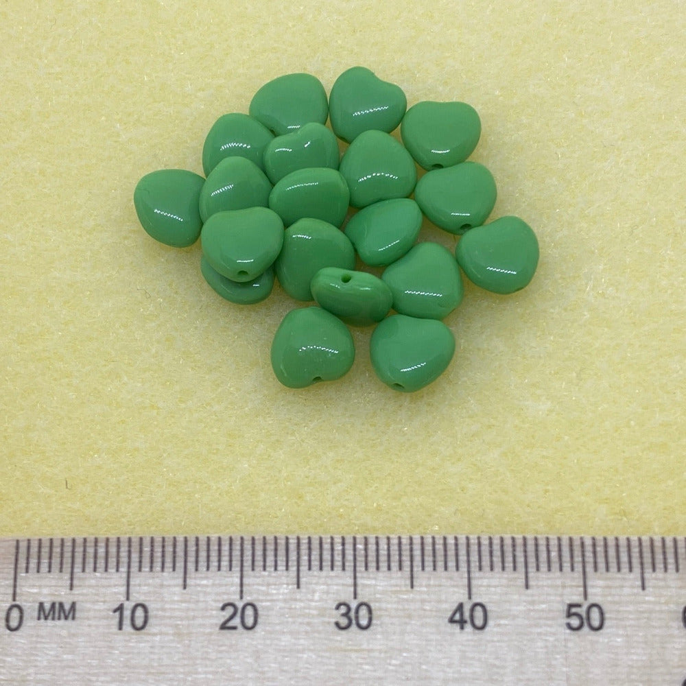 three green opaque heart beads in a group on a cream background with a ruler for scale