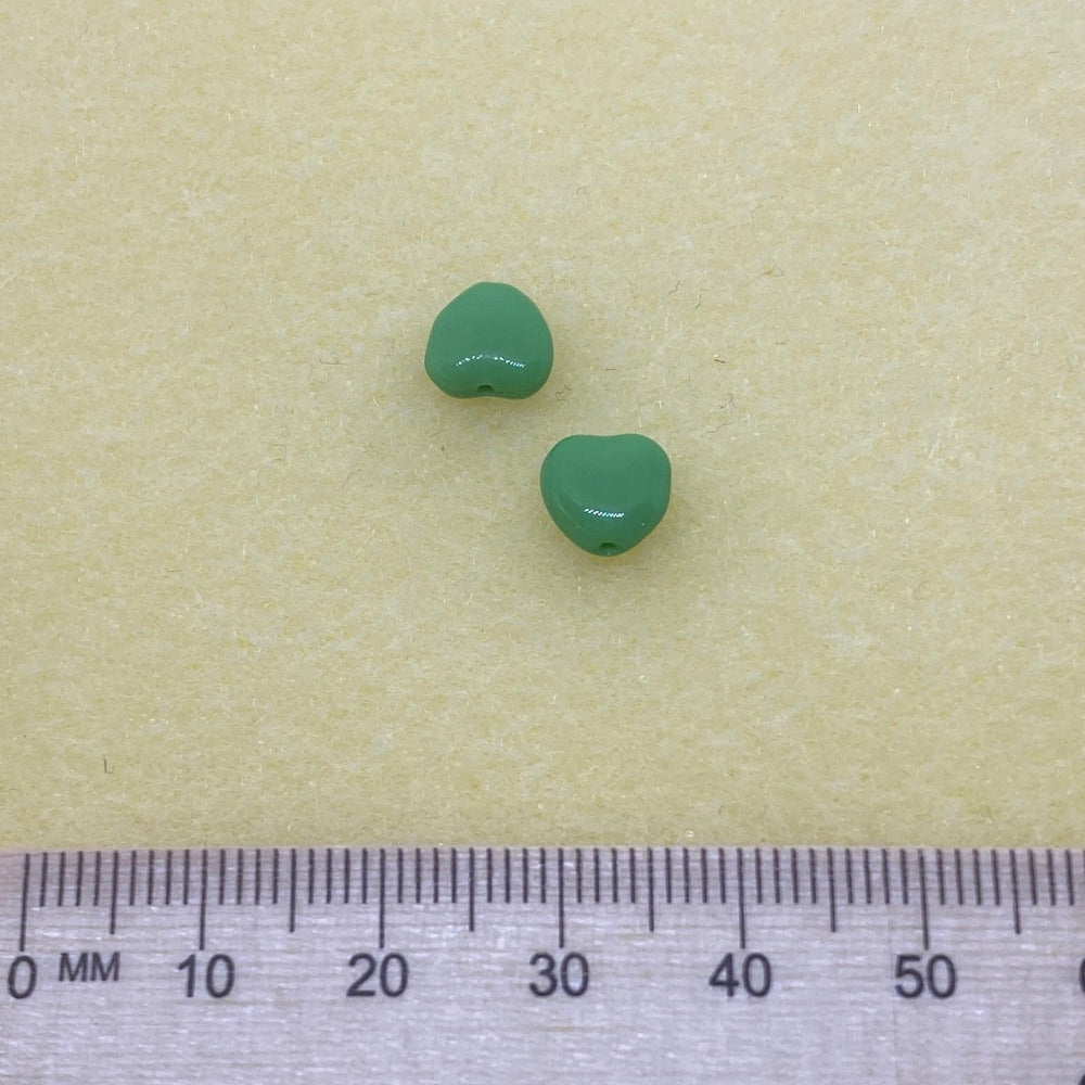 two green opaque heart beads threaded on a cream background with a ruler for scale