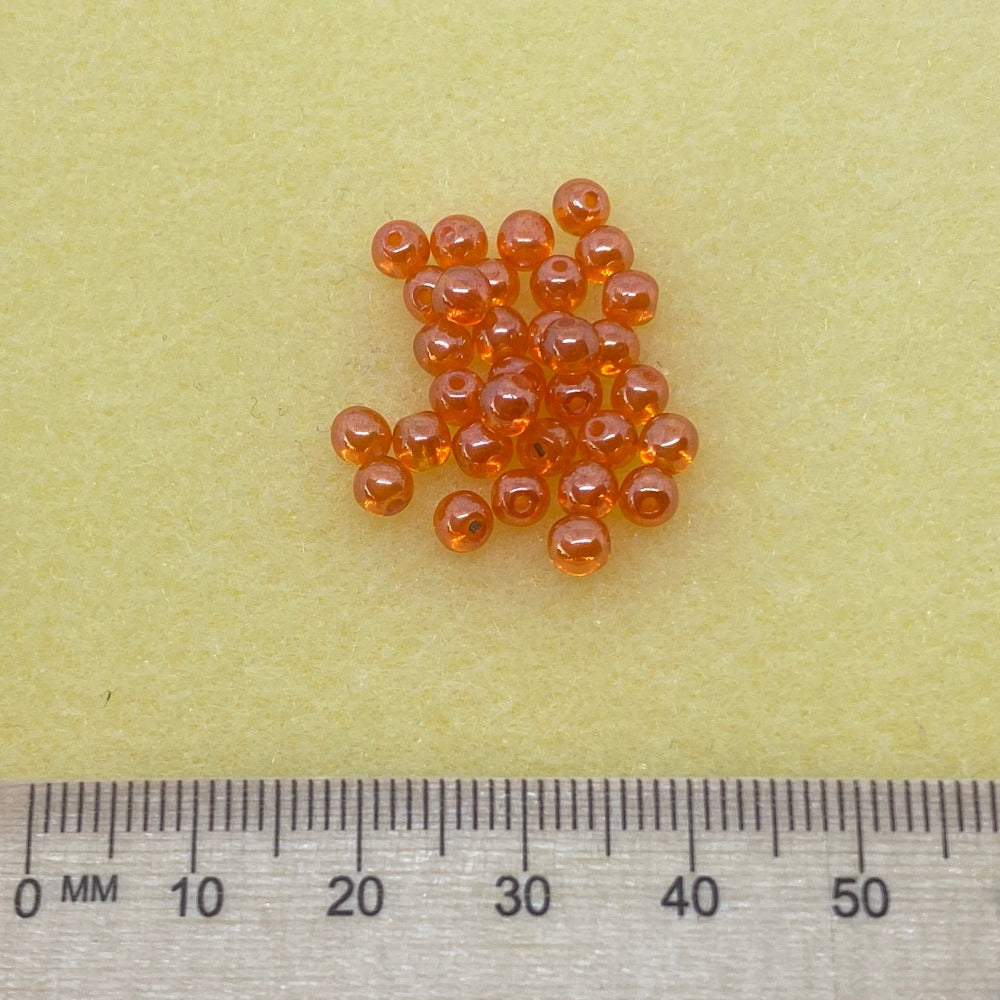 orange rainbow bubble style beads in a group on a grey surface showing threading holes for making necklaces