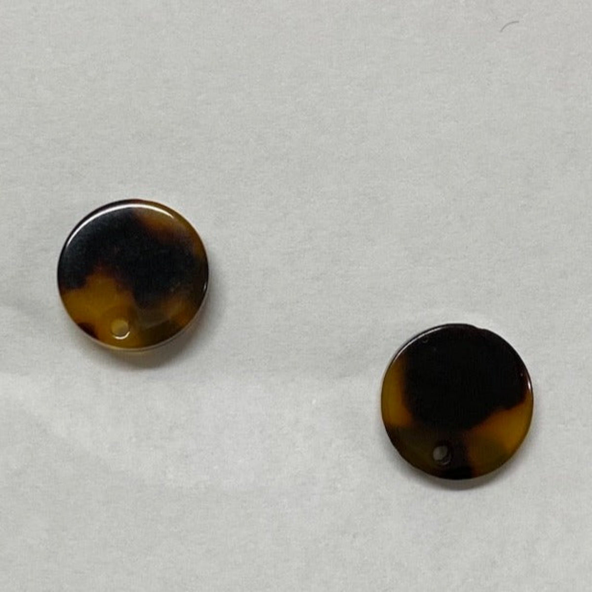 Two round, tortoise shell patterned stud attachments for earrings, with visible gold framing around the black enamel front.