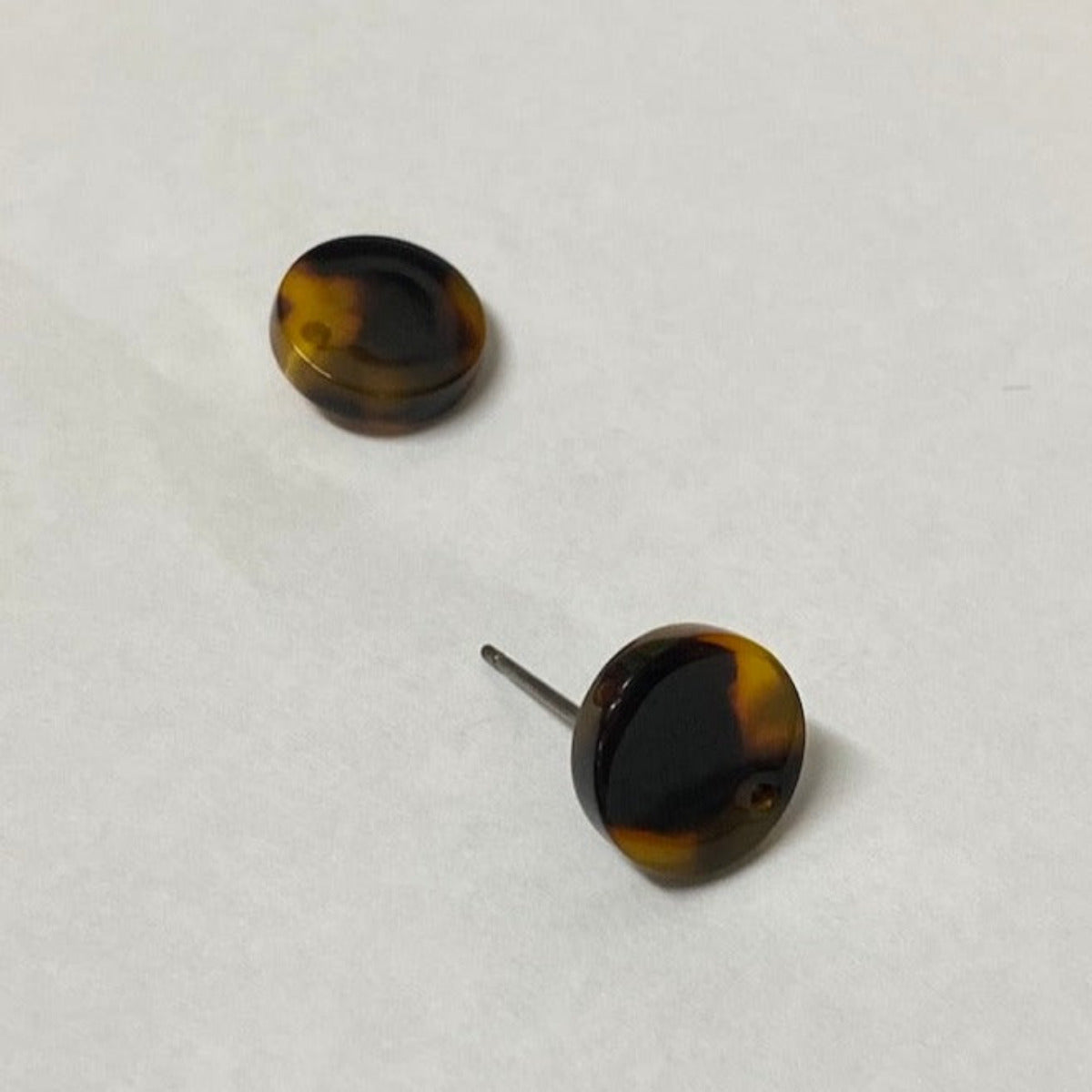Two round, tortoise shell patterned stud attachments for earrings, with visible gold framing around the black enamel front.