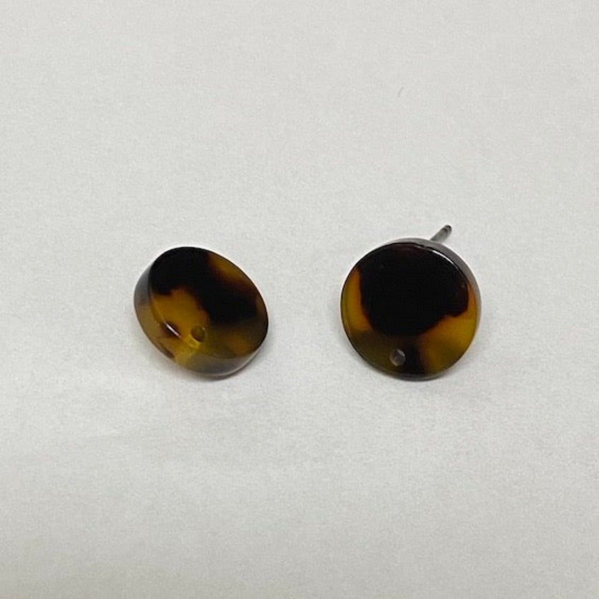 Two round, tortoise shell patterned stud attachments for earrings, with visible gold framing around the black enamel front.