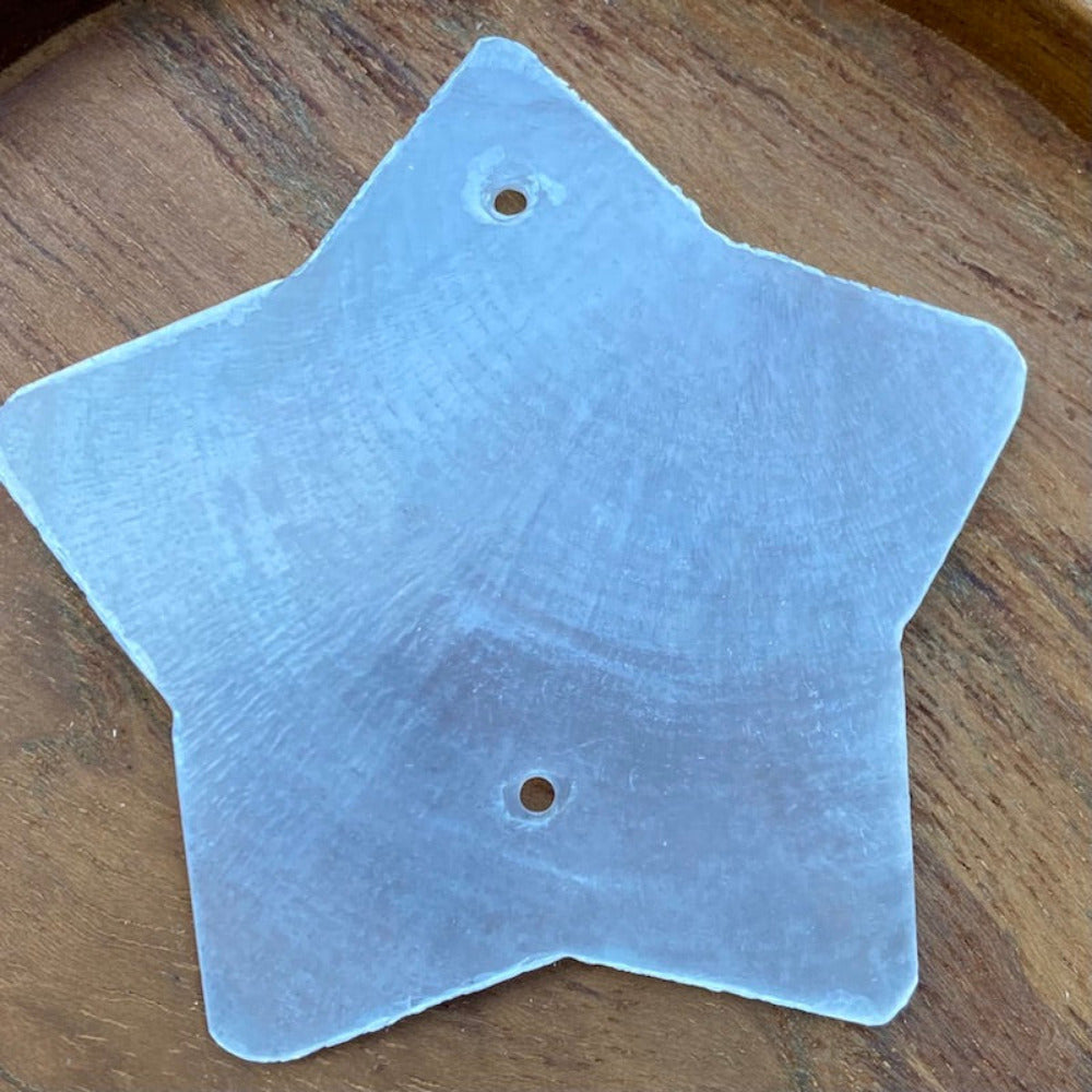a white star shaped capiz shell on a wood background for the purpose of making decor, craft and hanging decorations