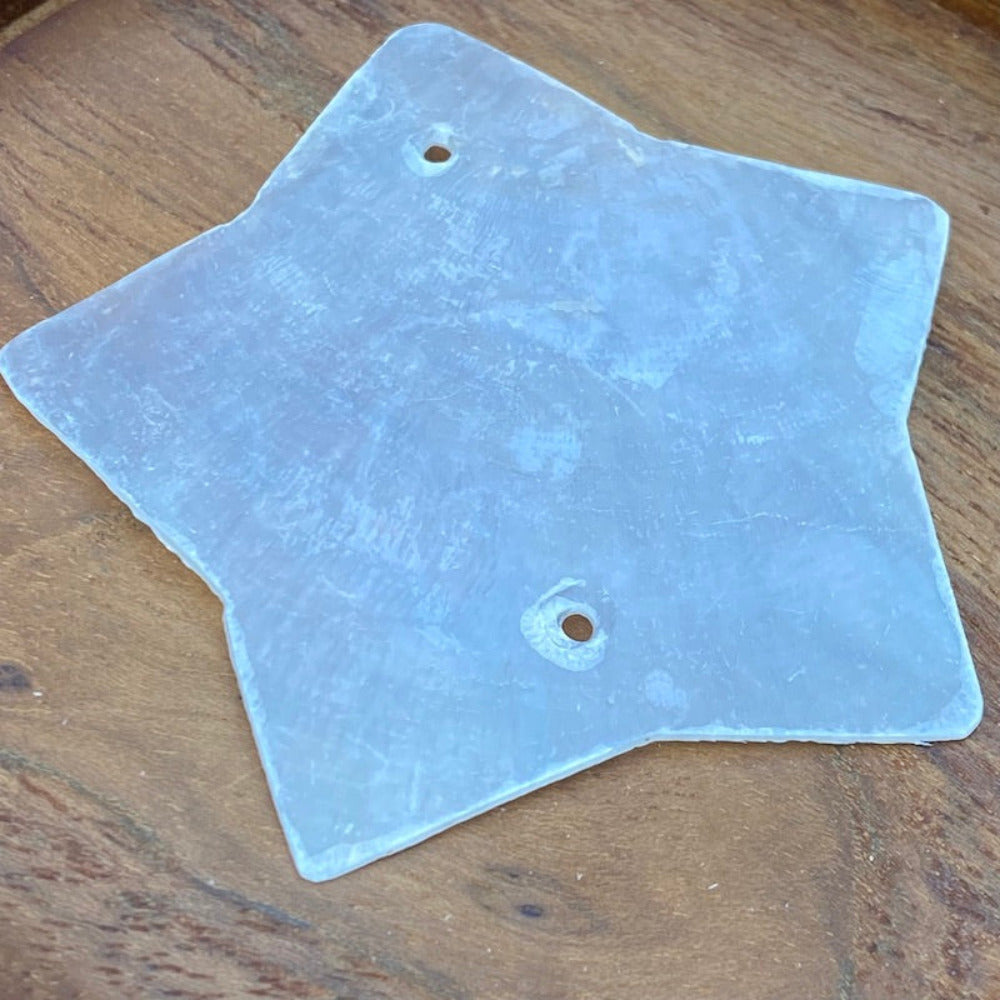 a white star shaped capiz shell on a wood background for the purpose of making decor, craft and hanging decorations