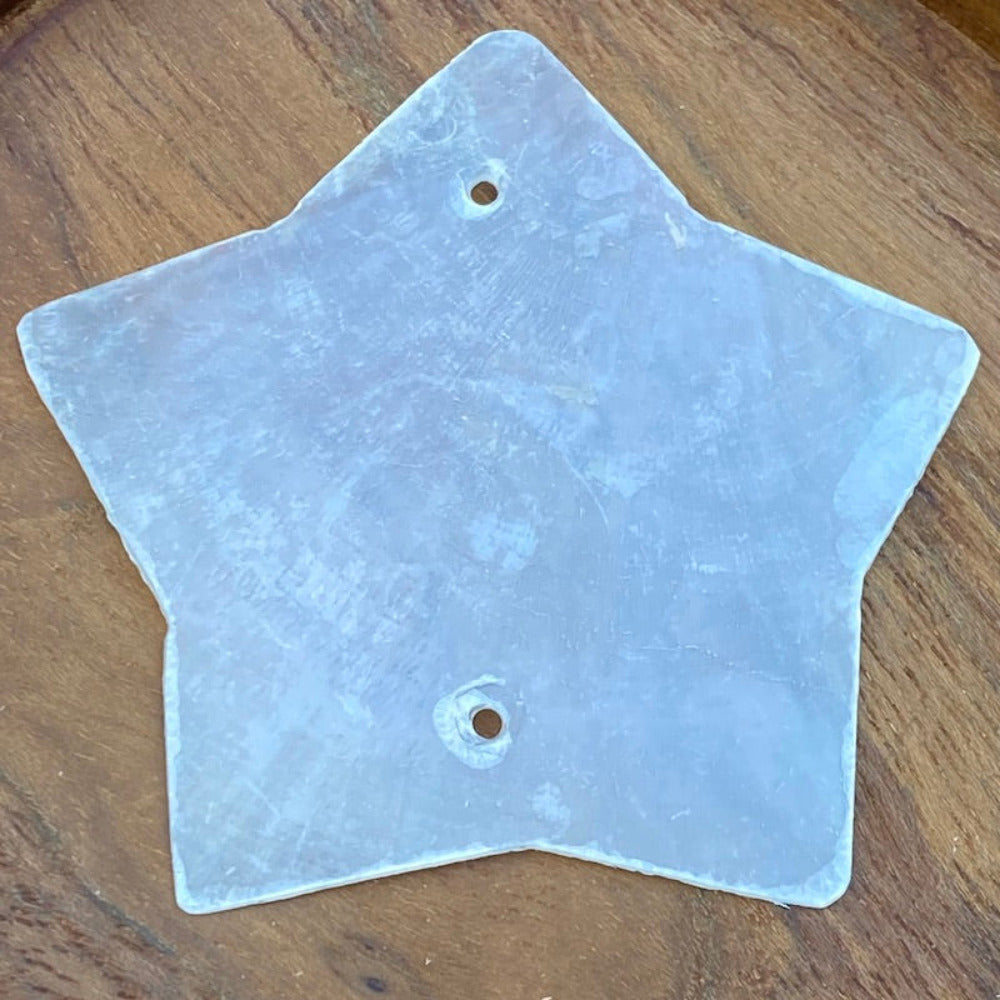 a white star shaped capiz shell on a wood background for the purpose of making decor, craft and hanging decorations