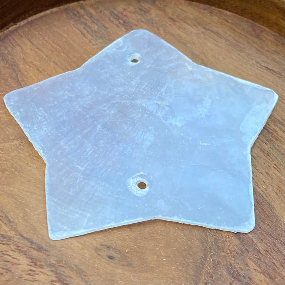 a white star shaped capiz shell on a wood background for the purpose of making decor, craft and hanging decorations