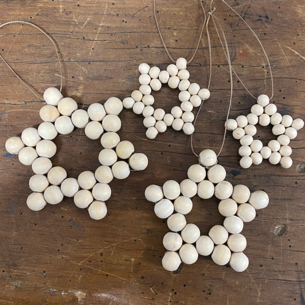 four decorative stars with raw wood beads and camel-colored flat waxed cord woven together displayed on a wood surface
