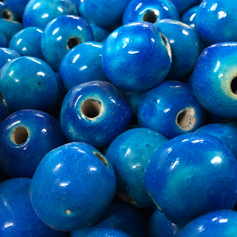 arge, round, cobalt blue vintage glazed ceramic beads with a visible hole in the center for threading, placed on a wooden surface.
