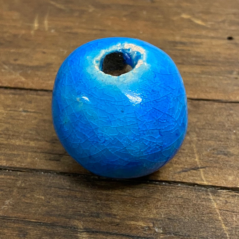 One large, round, cobalt blue vintage glazed ceramic bead with a visible hole in the center for threading, placed on a wooden surface.
