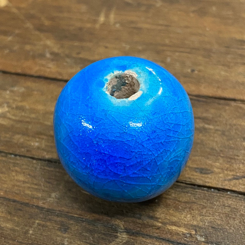 One large, round, cobalt blue vintage glazed ceramic bead with a visible hole in the center for threading, placed on a wooden surface.