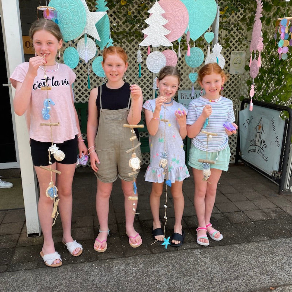Beautiful young girls proudly showing their beach themed hanging decorations made at the Bead Shack workshop for kids with hanging decorations in the background