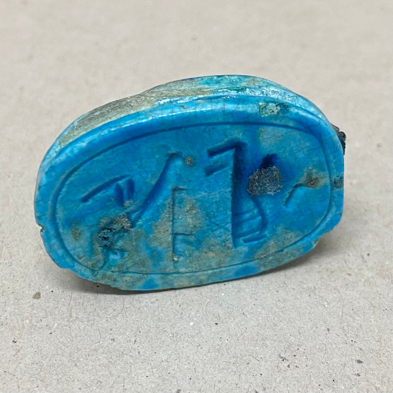 A vintage Egyptian scarab bead in blue color, displaying the reverse underneath side with Egyptian hieroglyphic markings