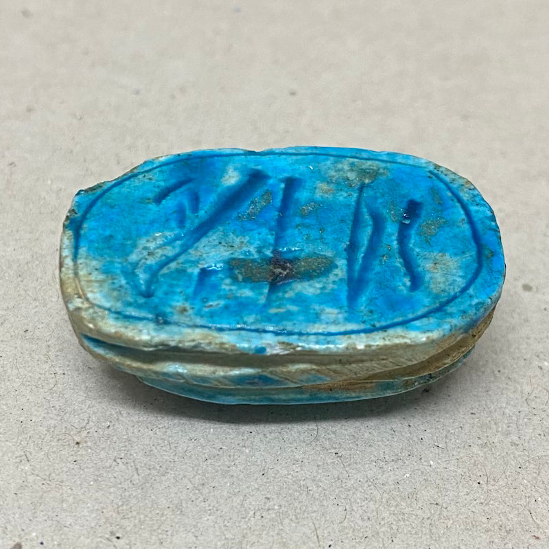 A vintage Egyptian scarab bead in blue color, displaying the reverse underneath side with Egyptian hieroglyphic markings