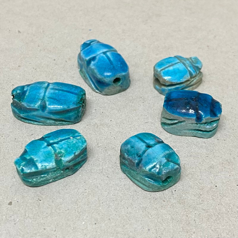 A collection of vintage Egyptian scarab beads in blue, varying slightly in size and shape, displayed against a neutral background.