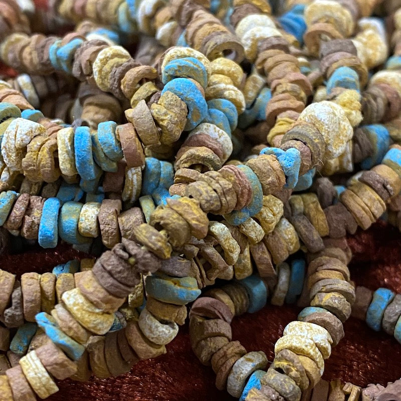 A close up photo of a collection of colored faience beads arranged in a loop, with varying shapes and textures.