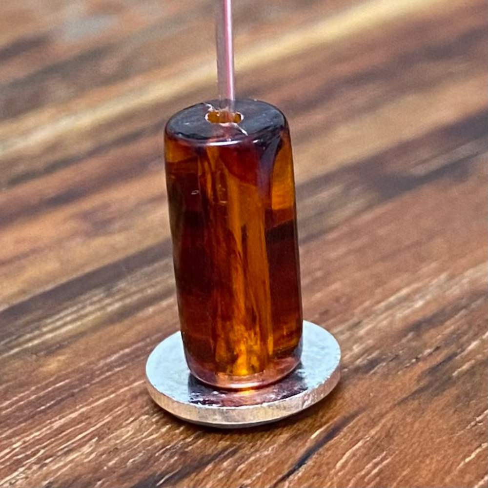 one transparent amber colour beads displayed on a wood surface with visible holes for stringing jewelry and creating craft