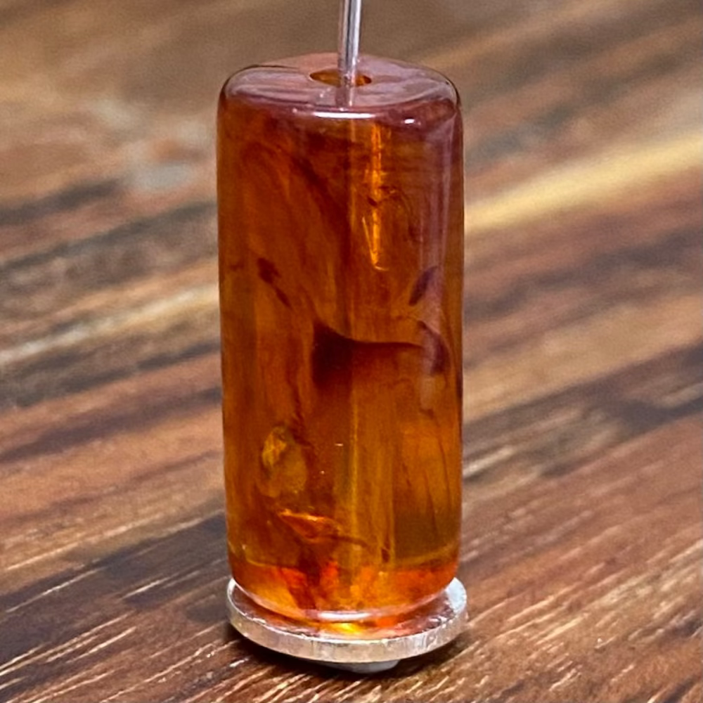 one tube shaped amber bead with black flecked markings on a wood background