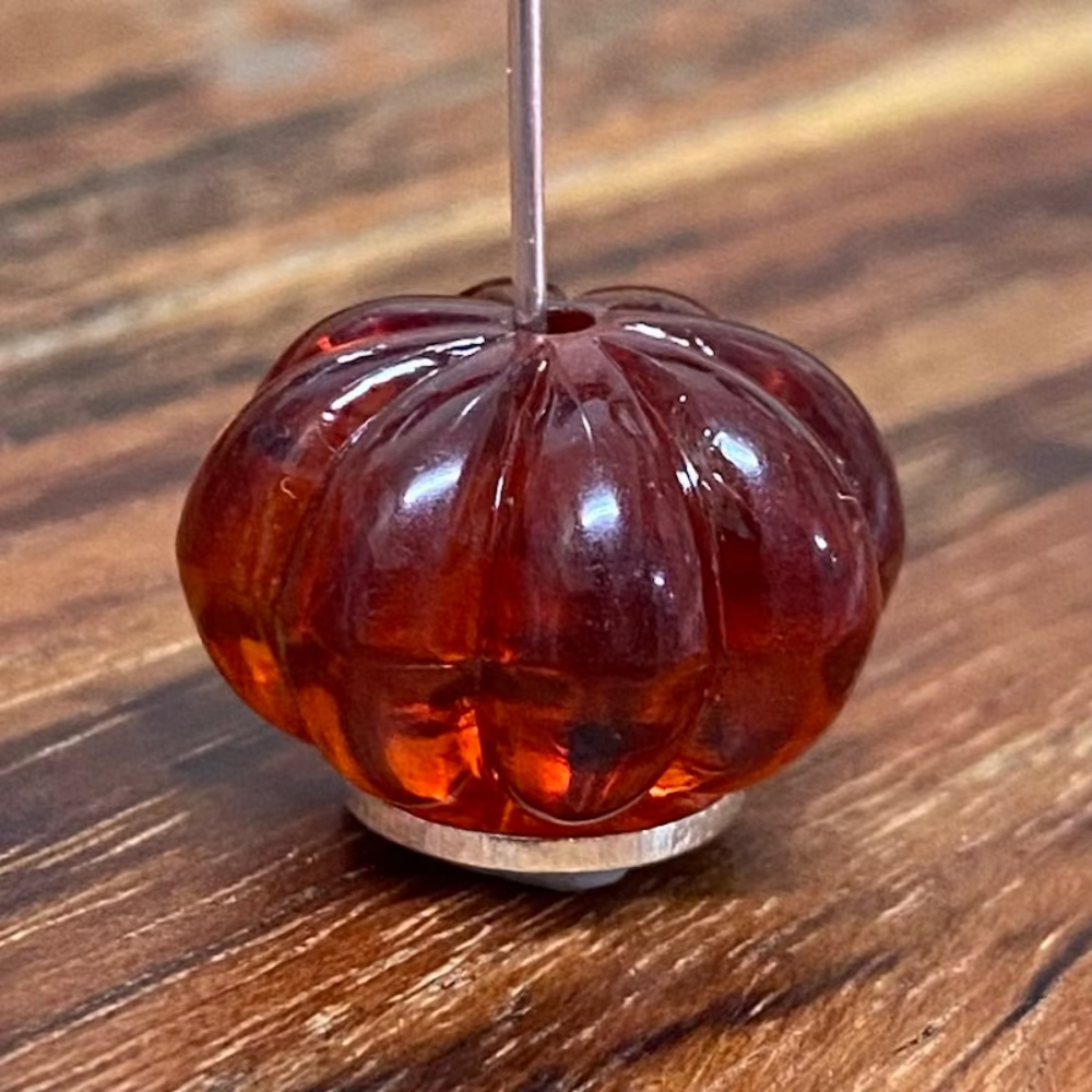 One transparent amber pumpkin shape beads with black markings, displayed on a wooden surface