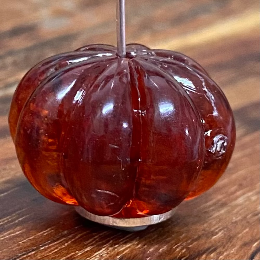 One transparent amber pumpkin shape beads with black markings, displayed on a wooden surface