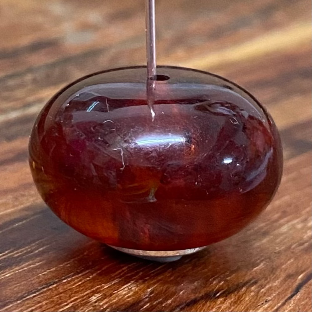 close up of one amber coloured transparent bead displayed on a pin with a wood surface in the background