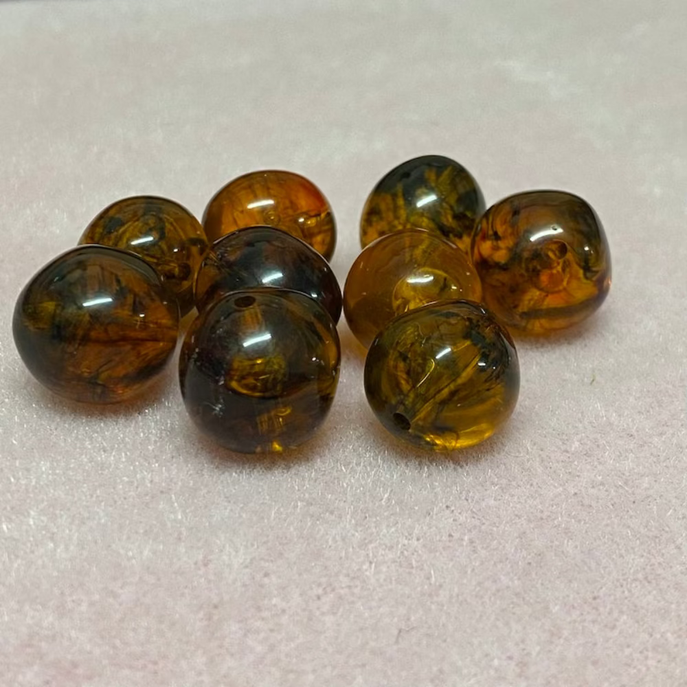 A collection of honey-colored amber beads with black markings, displayed on a pink surface