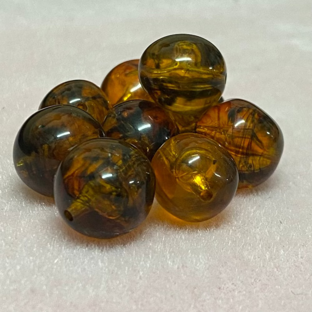 A collection of honey-colored amber beads with black markings, displayed on a pink surface
