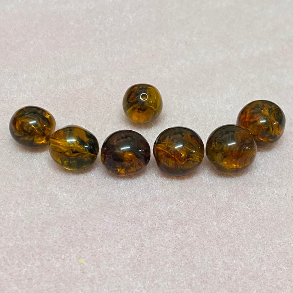 A collection of honey-colored amber beads with black markings, displayed on a pink surface