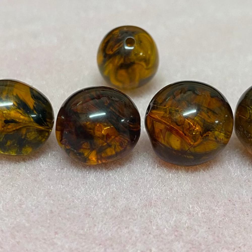 A collection of honey-colored amber beads with black markings, displayed on a pink surface