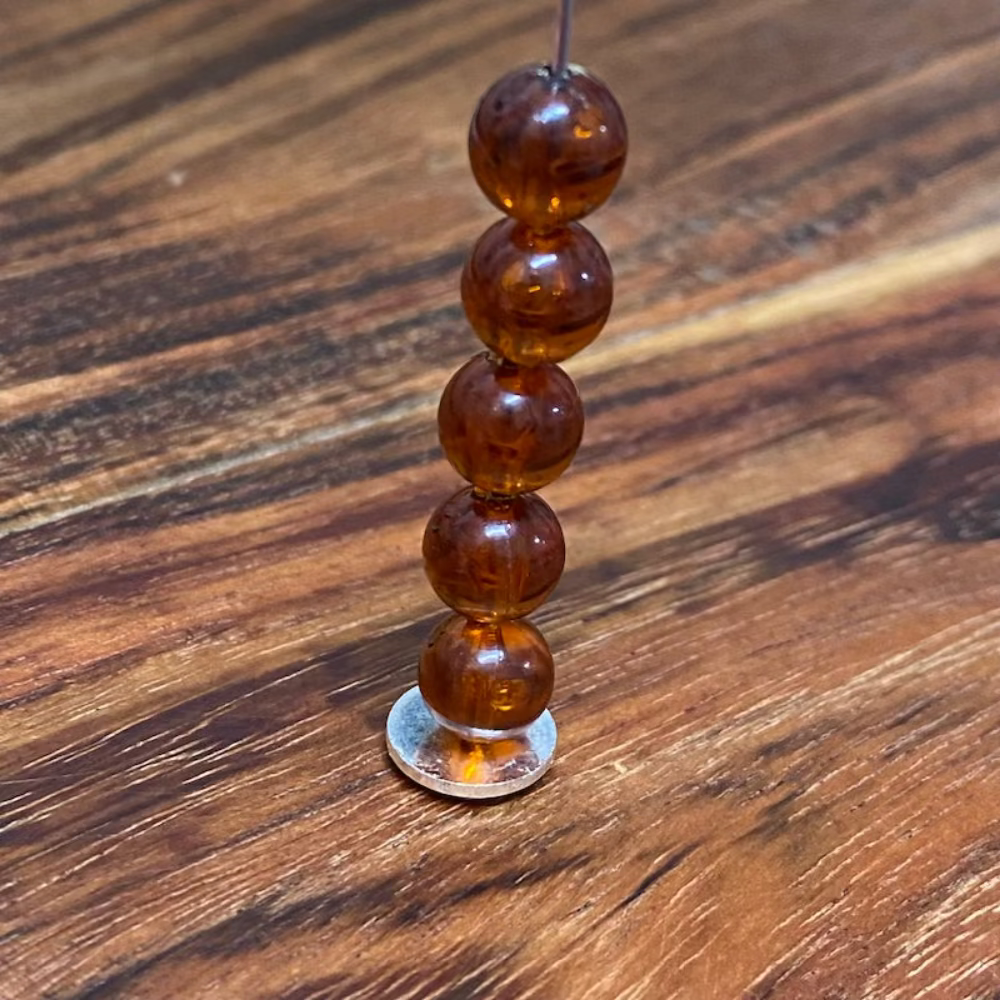 transparent amber beads on a pin with a wood surface in the background