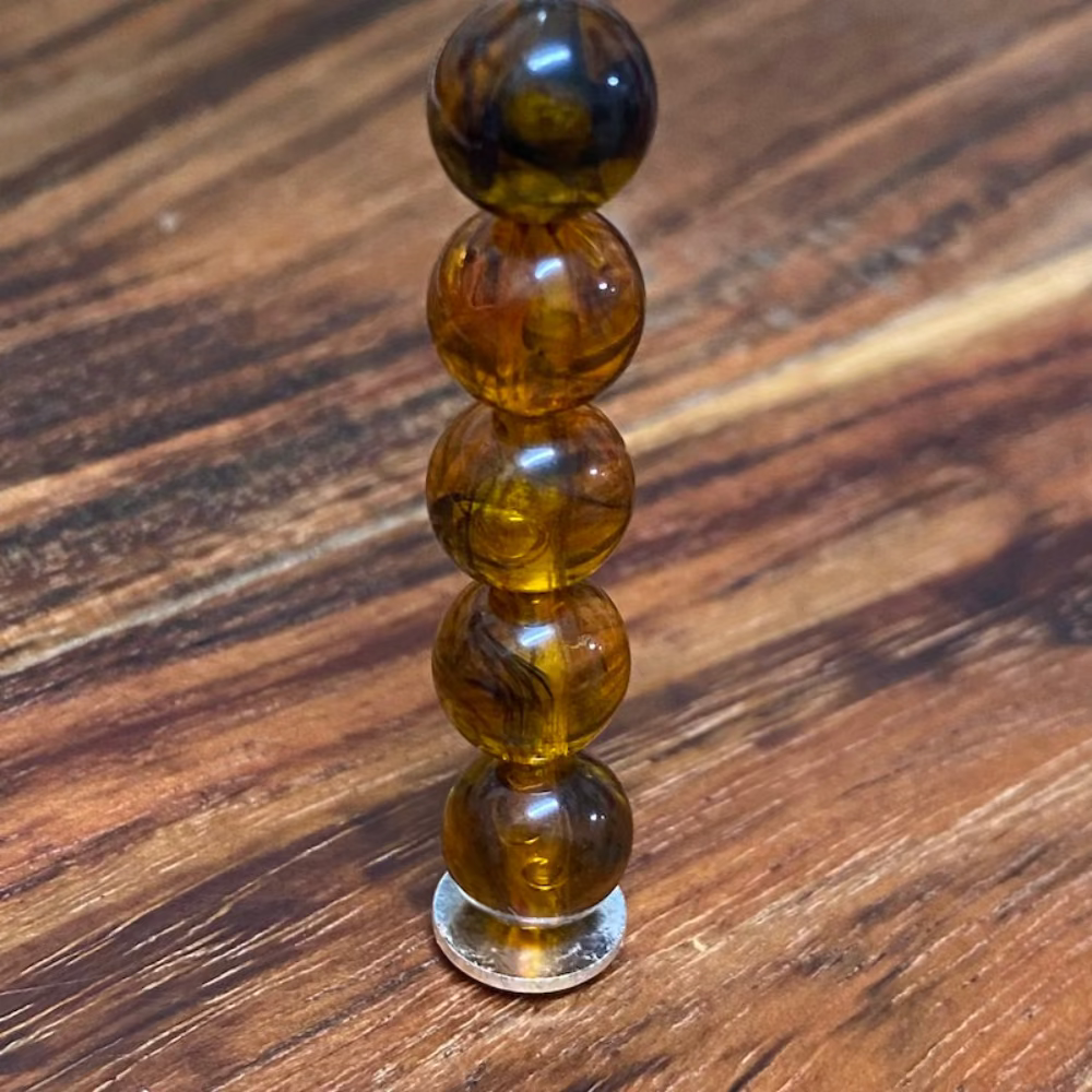 transparent amber beads on a pin with a wood surface in the background