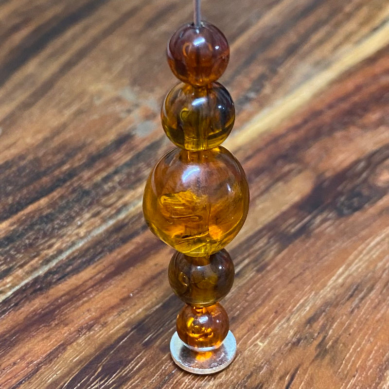 transparent amber beads on a pin with a wood surface in the background