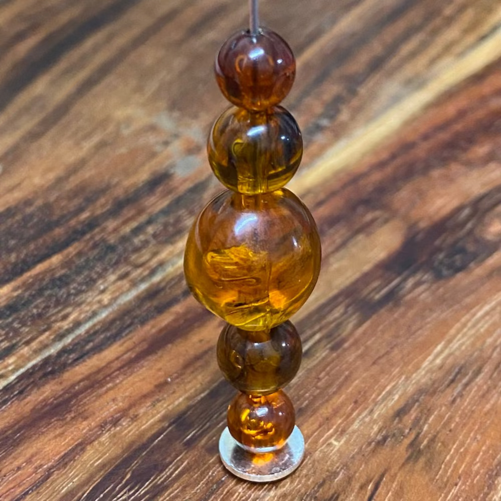 different sized transparent amber beads on a pin with a wood surface in the background