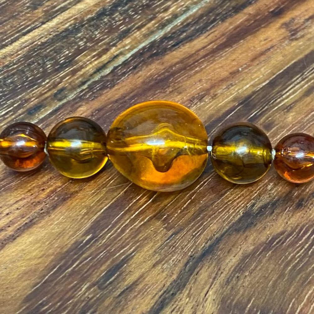 transparent amber beads on a pin with a wood surface in the background