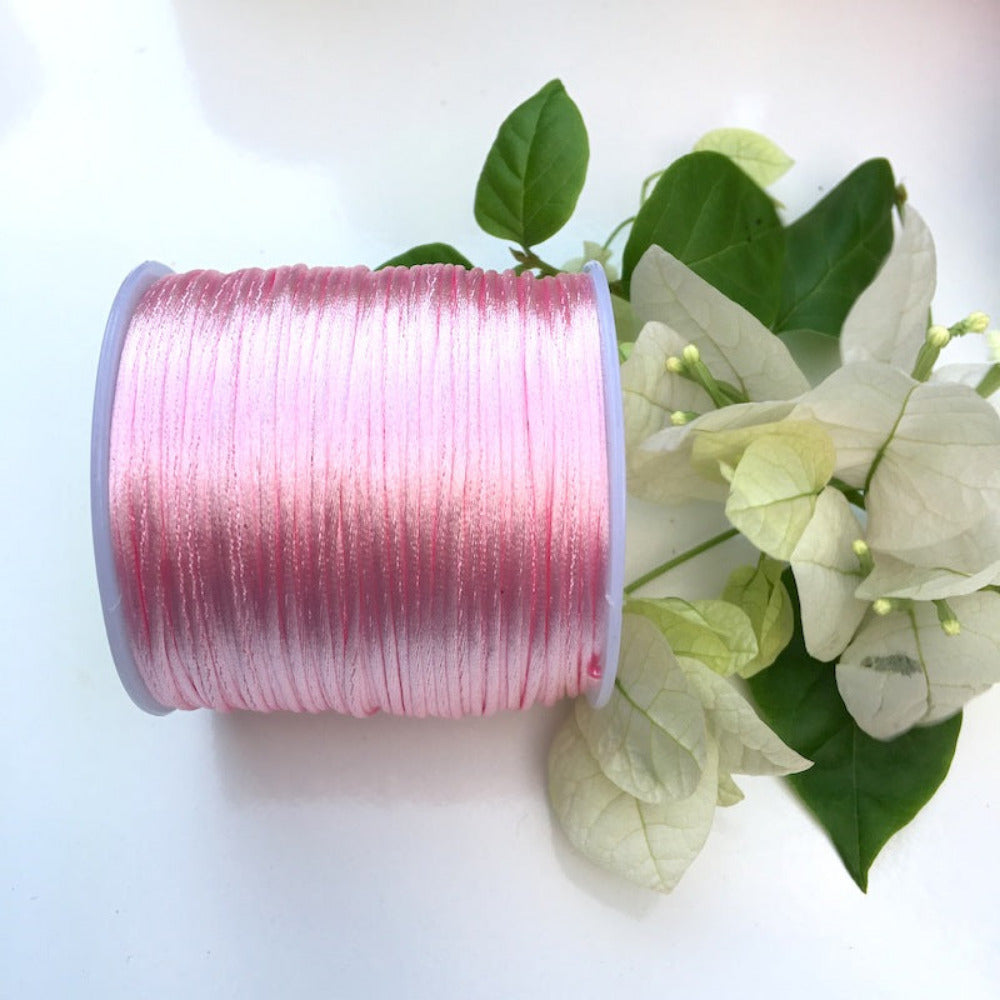 A spool of rat tail cord used for crafting, displayed alongside some white flowers and green leaves.
