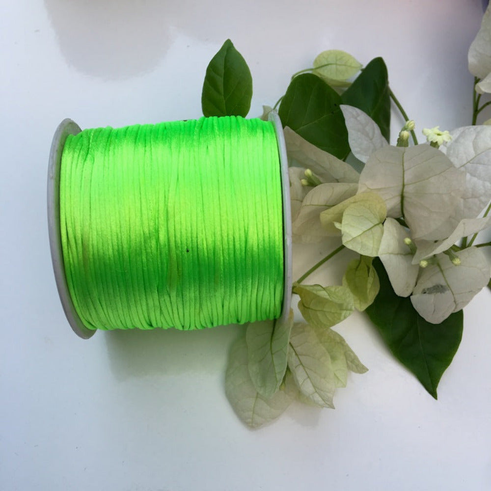 A spool of green rat tail cord next to some white flowers with green leaves on a white background.