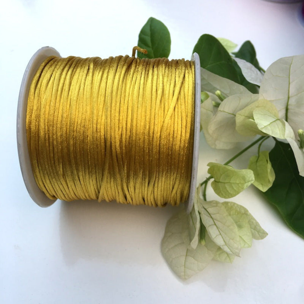 A spool of rat tail cord used for crafting, displayed alongside some white flowers and green leaves.