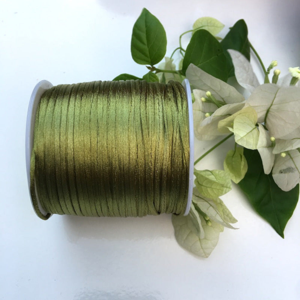 A spool of rat tail cord used for crafting, displayed alongside some white flowers and green leaves.