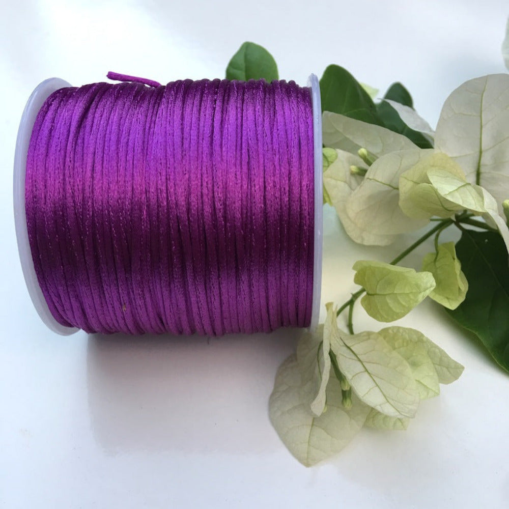 A spool of rat tail cord used for crafting, displayed alongside some white flowers and green leaves.