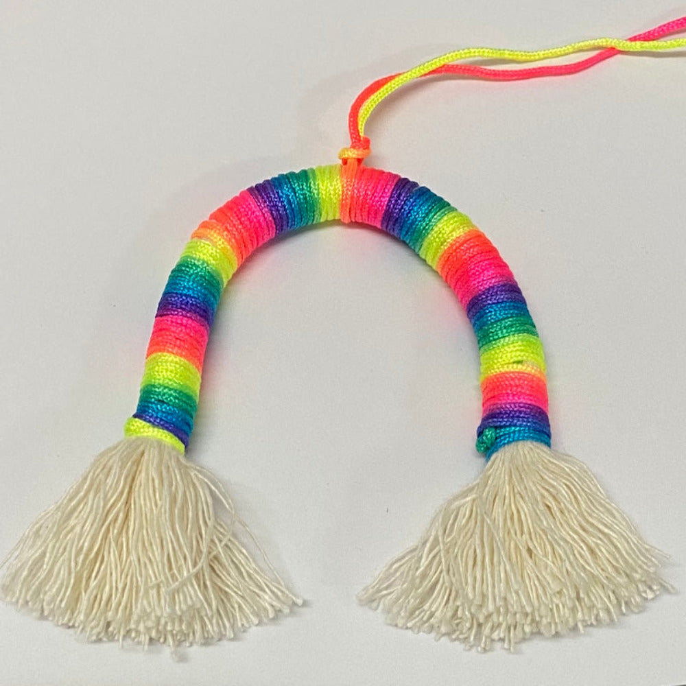 A completed Rainbow Decoration Kit with colorful yarn in a loop shape and white tassels on each end.