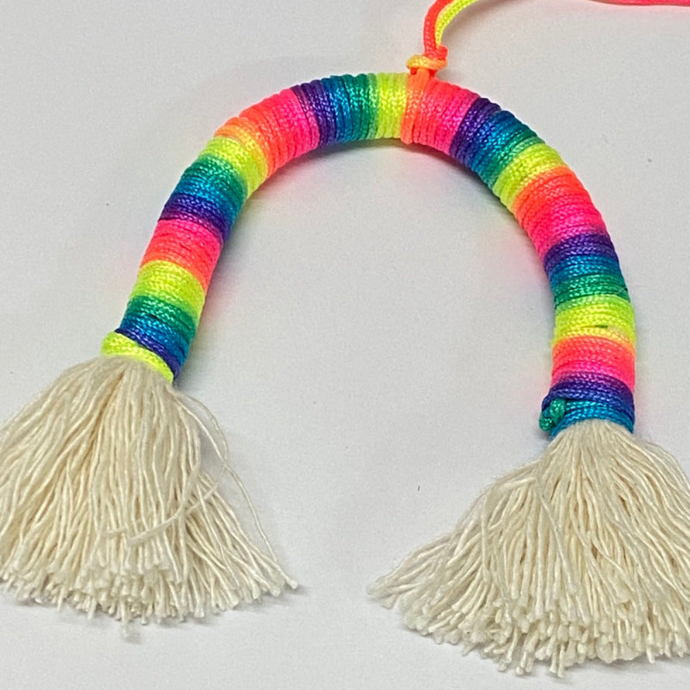 A completed Rainbow Decoration Kit with colorful yarn in a loop shape and white tassels on each end.