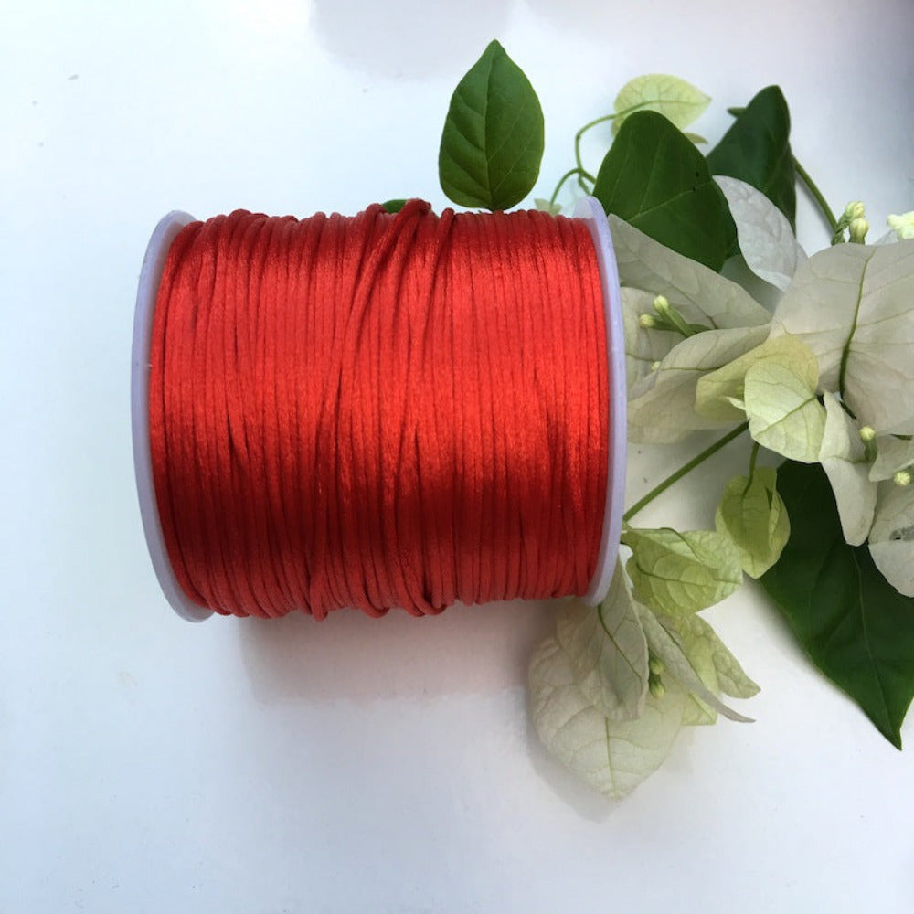 A spool of red rat tail cord used for crafting, displayed alongside some white flowers and green leaves.