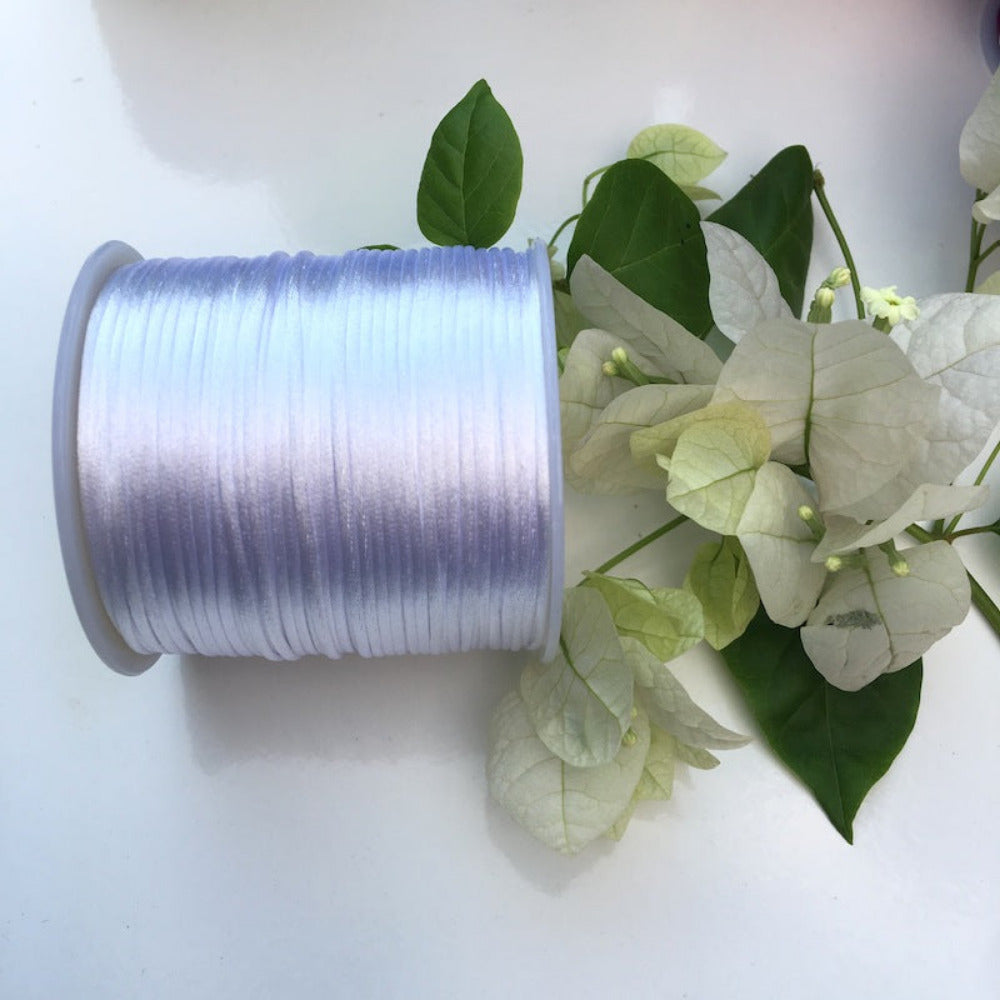 A spool of white rat tail cord used for crafting, displayed alongside some white flowers and green leaves.