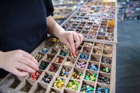 a wood tray of clay colourful beads with hands touching the beads