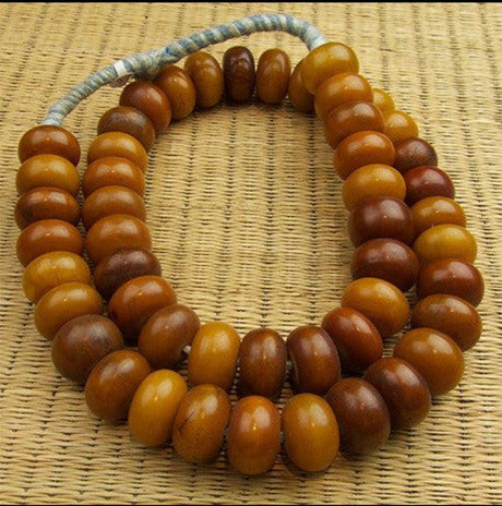 a beautiful example of dark amber and yellow coloured phenolic amber beads on a string shown on a wicker surface