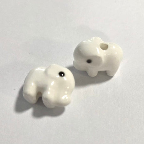 Two white ceramic elephant beads on a light gray background