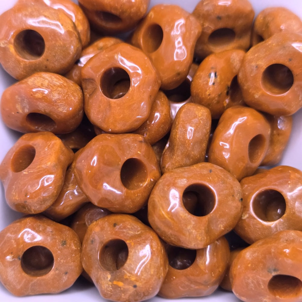 Close-up of orange beads with holes on a white background